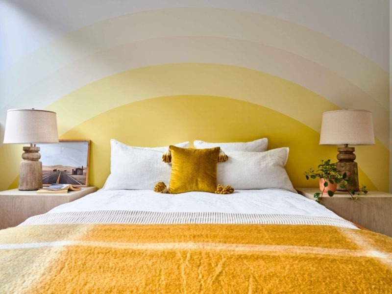 Không gian phòng ngủ của chủ nhà mệnh Thổ với bức tường được sơn cách điệu như hình mặt trời cùng bộ chăn ga màu cam - nâu bắt mắt